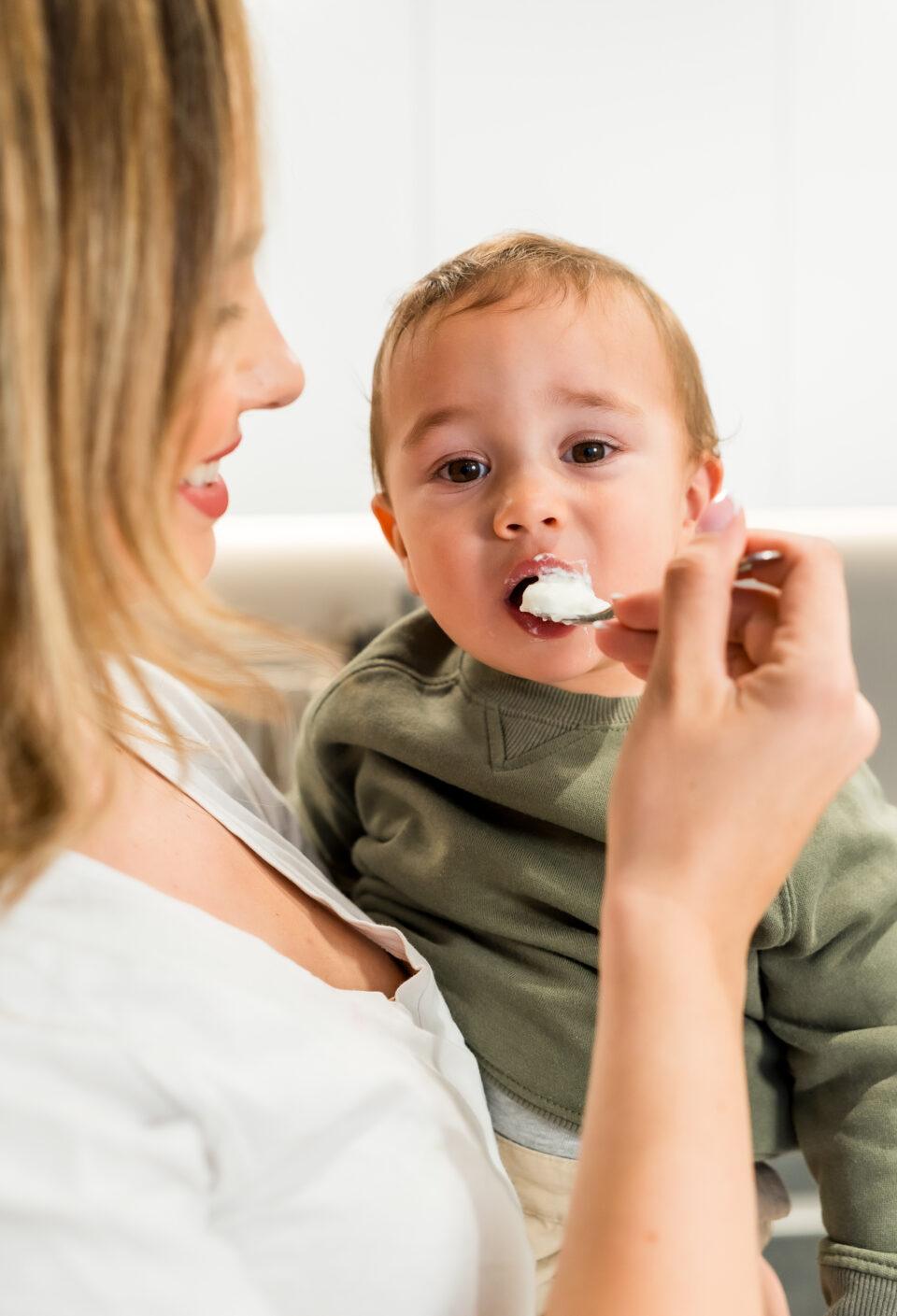 Mother feeding her baby son with yogurt in a spoon in the kitchen Mother feeding her baby son with yogurt in a spoon in the kitchen