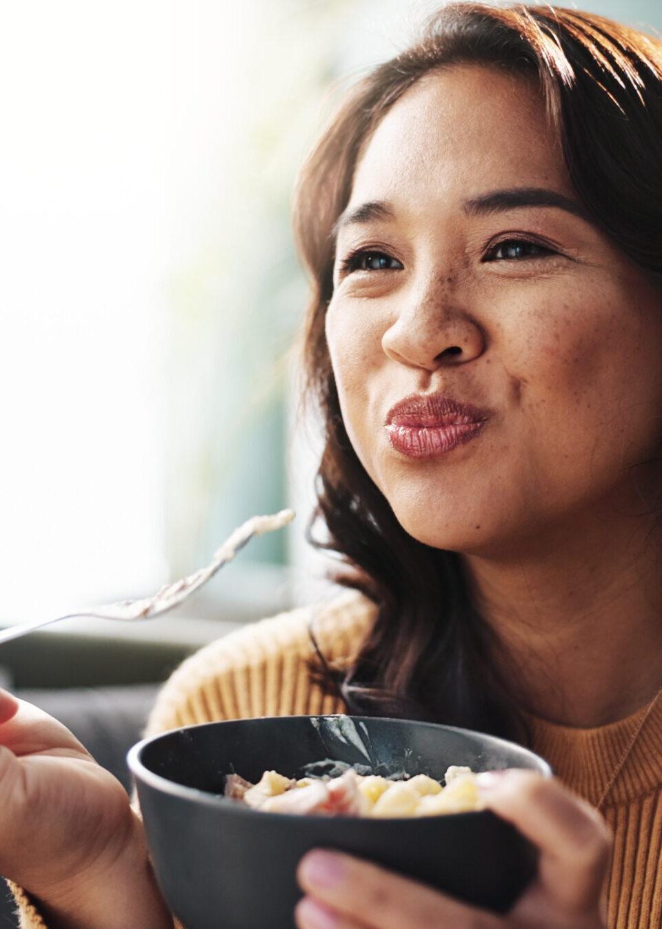 Happy, woman and eating food on sofa for dinner meal, nutrition and enjoyment with relax. Wellness snack, person and hungry with pasta bowl in living room for healthy diet, weekend break and cuisine Happy, woman and eating food on sofa for dinner meal, nutrition and enjoyment with relax. Wellness snack, person and hungry with pasta bowl in living room for healthy diet, weekend break and cuisine