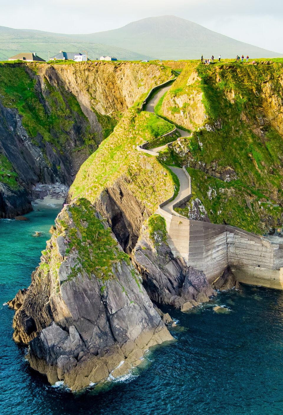 Dunquin or Dun Chaoin pier, Ireland's Sheep Highway. Aerial view of narrow pathway winding down to the pier, ocean coastline, cliffs. Popular location on Slea Head Drive and Wild Atlantic Way. Dunquin or Dun Chaoin pier, Ireland's Sheep Highway. Aerial view of narrow pathway winding down to the pier, ocean coastline, cliffs. Popular location on Slea Head Drive and Wild Atlantic Way.