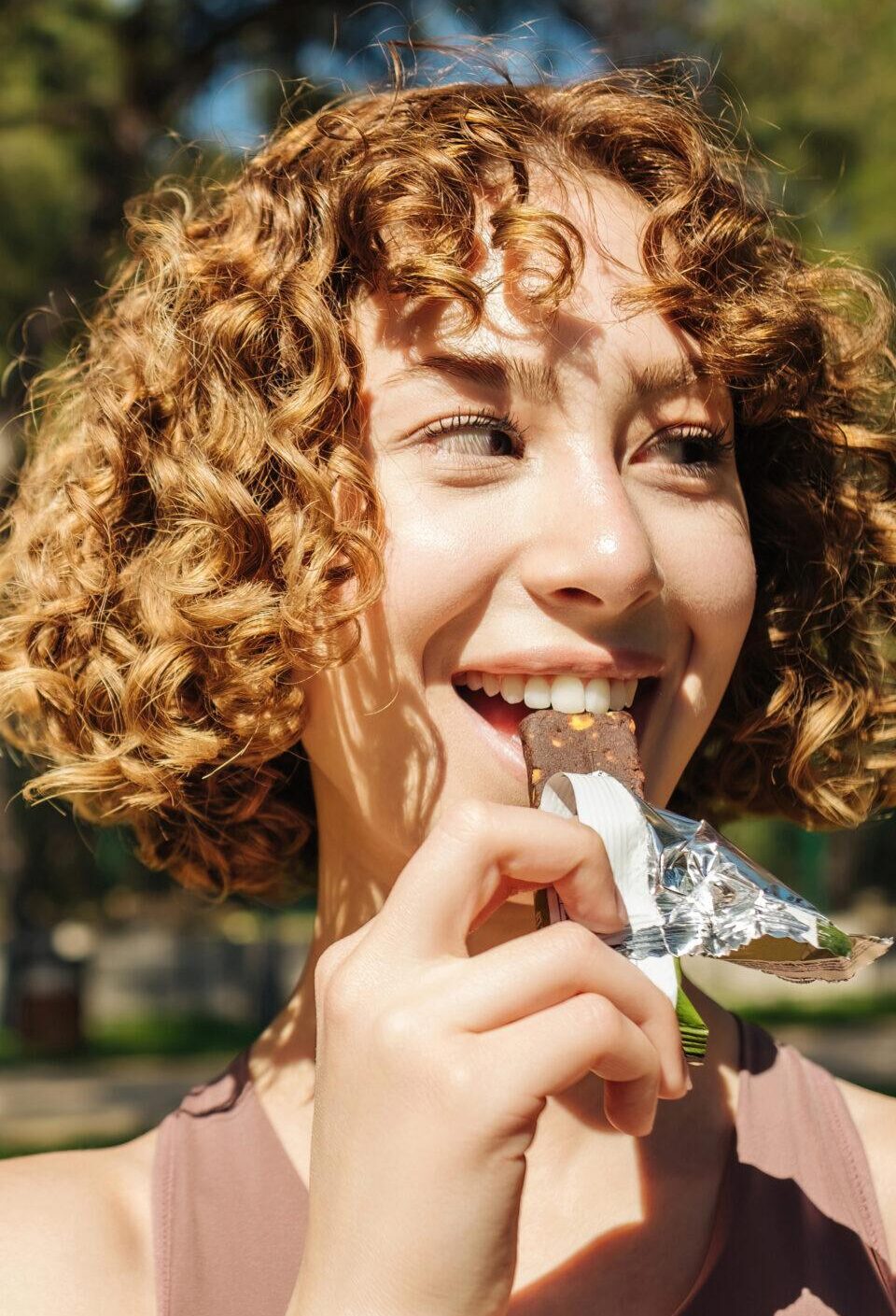 Athletic woman eating a protein bar. Fitness beautiful woman eating a energy snack outdoor. Copy space. Healthy food, outdoor sports concepts.