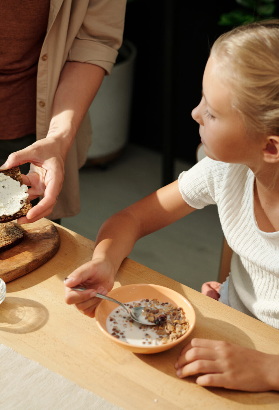 Youthful girl eating muesli with milk and looking at her mother making sandwich Youthful girl eating muesli with milk and looking at her mother making sandwich
