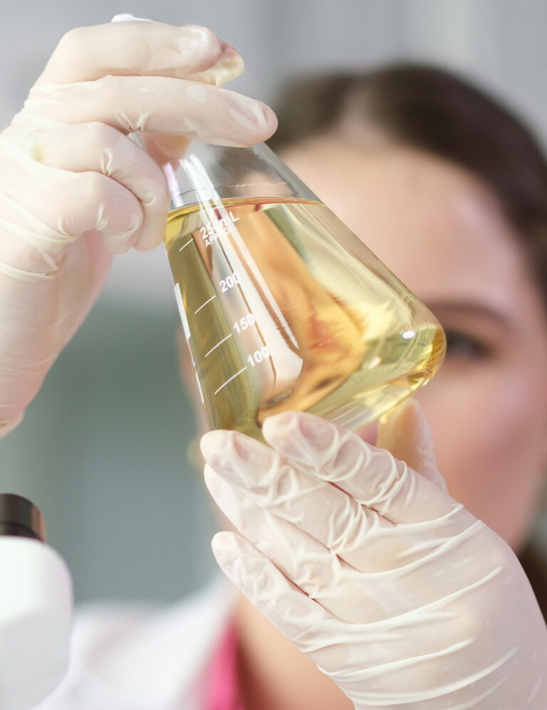 Scientist chemist looking at flask with yellow brake oil in chemistry lab closeup Scientist chemist looking at flask with yellow brake oil in chemistry lab closeup
